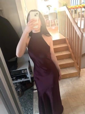 Burgundy balklänning slutsåld helt ny - Säljer en elegant långklänning i burgundy med halterneck och figurnära passform. Klänningen har en slät, glansig yta och är ärmlös, vilket ger en stilren och modern look. Perfekt för balen. Den är helt ny och slutsåld på hemsidan. 