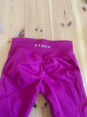 Mörkrosa seamless leggings GTECH - Snygga mörkrosa seamless leggings från GTECH med hög midja och bred resår. Materialet är stretchigt och följsamt, perfekt för träning eller chill. Diskret logga framtill i midjan. Tight passform och scrunch-detalj bak.