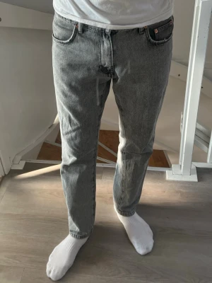 Grå raka jeans från Woodbird - Säljer ett par grå raka jeans från Woodbird med klassisk femficksdesign och knappgylf. Jeansen har en snygg tvättad look och är tillverkade i bomull. Perfekta för en avslappnad och trendig stil. W30 L32
