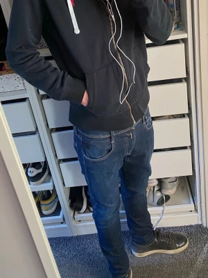 Replay Anbass - Säljer ett par mörkblå jeans från Replay med klassisk femficksdesign och vit kontrastsöm på bakfickan. Jeansen har normal midja och smal passform, perfekta till sneakers. Materialet är mjukt denim med lite stretch för extra komfort. Modellen är 180cm