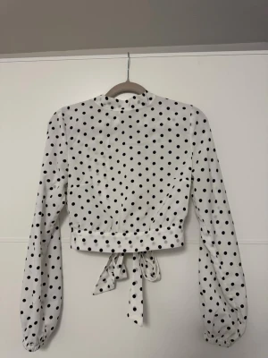 Vit prickig blus med knytband - Supersöt vit blus med svarta prickar och långa ärmar. Blusen har knytband både i midjan och vid halsen, samt lätt puffade ärmslut. Perfekt för dig som gillar en trendig stil👀❤️