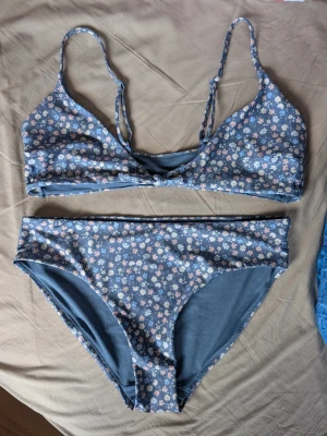 Blommig blå bikini från Kappahl - Säljer en söt bikini från Kappahl i storlek M. Den är blå med små blommor i ljusrosa, vit och ljusblå. Bikinin knyts fram. Utan iläggskupor. 