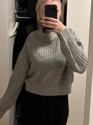 Grå stickad tröja med grov struktur - Säljer en grå stickad tröja med grov struktur och rund hals. Tröjan har långa ärmar och ribbade muddar vid ärmslut och nederkant. Perfekt för lager-på-lager och chill dagar.