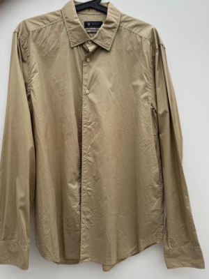 Beige skjorta från Riley - Klassisk beige skjorta från Riley med lång ärm och enkel krage. Skjortan har knäppning framtill och är perfekt som vardagsskjorta. 