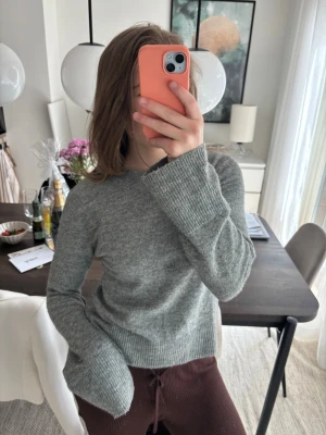 Grå stickad tröja med vida ärmar - Mysig grå stickad tröja med rund hals och vida, ribbstickade ärmar. Tröjan har en enkel design och är tillverkad i ett mjukt material som passar perfekt för kyliga dagar. Perfekt att matcha med jeans eller mjukisbyxor.