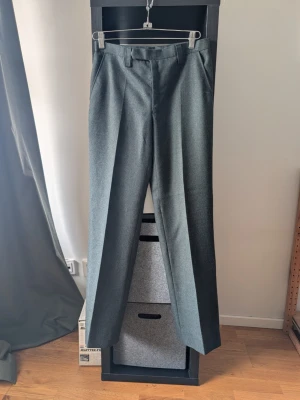 Mörkgröna kostymbyxor i ull - Stilrena mörkgröna kostymbyxor med pressveck och hällor för bälte. Byxorna har rak passform och är tillverkade i ett ulligt tyg som ger en klassisk look. Perfekta för dig som vill ha en dressad stil med en twist.