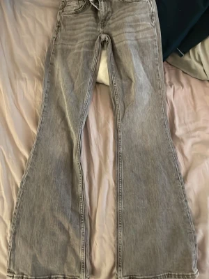 Gråa bootcut jeans med utsvängda ben - Säljer ett par gråa bootcut jeans med riktigt snygg utsvängd passform. Jeansen har klassisk femficksdesign och är gjorda i denim. Perfekta för dig som gillar retrovibbar och vill ha ett par jeans som sticker ut lite extra.