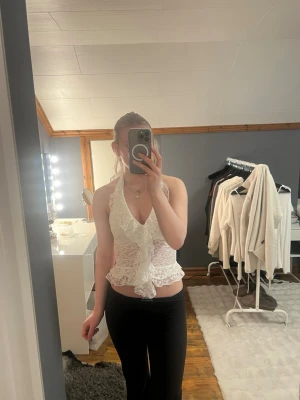 Vit spetsig omlott halterneck topp - Säljer en vit ärmlös halterneck topp i spets med omlottdesign och volangdetalj framtill. Toppen knyts i nacken och har öppen rygg. Toppen är från Shein.