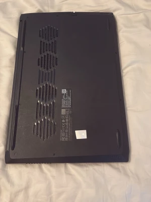 Svart Lenovo bärbar dator - Snygg och stilren svart bärbar dator från Lenovo med en slimmad design. Locket är matt och har en diskret Lenovo-logga i hörnet. Undersidan har flera ventilationsgaller för bra kylning. Perfekt för studier, gaming eller vardagsanvändning.