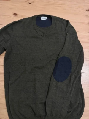 Olivgrön tröja - John Henric - Olivgrön  tröja från John Henric med V-ringning och blå armbågslapp på ena ärmen.  Dålig bild så snyggare i verkligheten. Den är knappt använd! Bara att skriva vid frågor.
