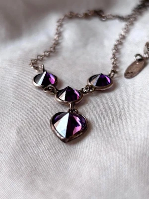 Silverhalsband med lila hjärthänge - Snyggt silverhalsband med tre runda lila ametist stenar i form av hjärtan. Kedjan är tunn och har justerbar längd. 925 och GHA stämplad