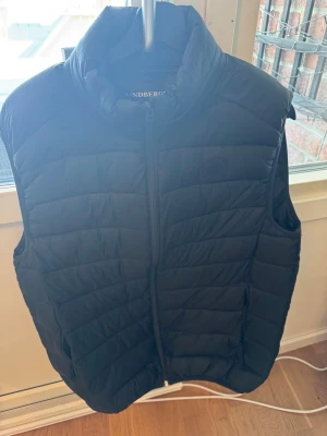 Svart dunväst från J.Lindeberg - Snygg svart dunväst från J.Lindeberg med hög krage och dragkedja framtill.