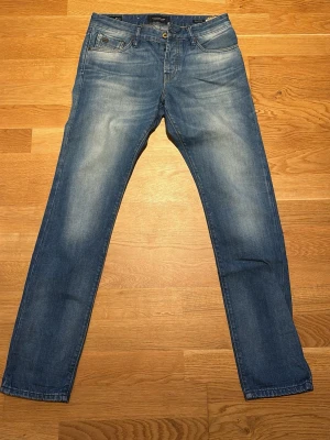 Ljusblå raka jeans från Scotch & Soda - Säljer ett par ljusblå jeans från Scotch & Soda (Ralston) med raka ben och klassisk femficksmodell. Jeansen har snygga slitningar och kontrastsömmar från fabrik, samt en liten logga på myntfickan. Perfekta för en avslappnad och trendig look. Strl 30/32