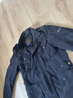 Mörkblå vindjacka från Woolrich - Säljer nu denna snygga vindjackan från märket Woolrich! Jackan är i ett skönt material som passar utmärkt nu under våren! Jackan är i ett använt skick men fortfarande mycket kvar att ge! Storlek S, hör av er vid frågor! 