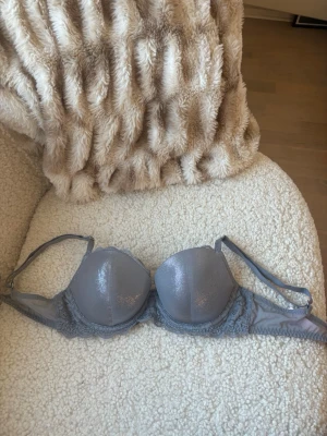 Grå glittrig bh från Victoria's Secret - Snygg glittrig bh från Victoria's Secret med glittrig finish och spetsdetaljer längs kanterna. Bh:n har justerbara axelband och bygel för extra stöd. Perfekt för dig som vill ha något extra fint under kläderna.