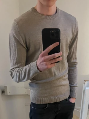 Beige stickad tröja  - En stilren beige stickad tröja med rund halsringning och ribbade muddar vid ärmslut och nederkant. Perfekt basplagg för lager på lager och enkel att matcha med olika outfits. Tröjan har en klassisk passform och är mjuk i materialet.