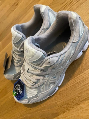 Vita Asics sneakers med mesh och skinn - Snygga vita sneakers från Asics med detaljer i ljusgrått. Skorna har en sportig design med ovandel i mesh och syntetiskt skinn, samt en rejäl sula för extra komfort. Perfekta för dig som gillar en clean och modern look.