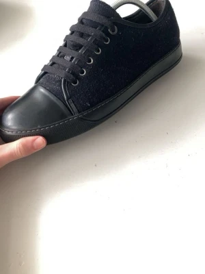 Två par stilrena sneakers i mörka färger - Säljer två par sneakers med lågt skaft. Ena paret är svart med gummitå och textilovandel, det andra är mörkgrönt med brunt tåparti och vit sula, troligtvis i mocka och läder. Båda har klassisk snörning och passar perfekt till en clean streetstyle.