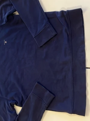 Mörkblå sweatshirt från GANT - Klassisk mörkblå sweatshirt från GANT med rund halsringning och diskret logga broderad på bröstet. Tröjan har ribbade muddar vid ärmslut och nederkant samt en mjuk bomullskänsla. Perfekt för en avslappnad och stilren look.