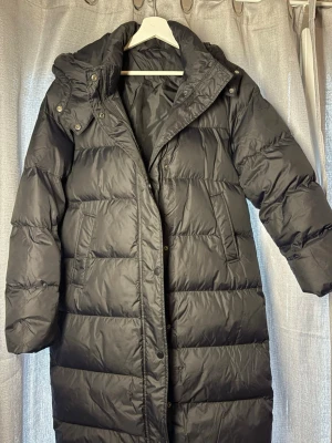 Svart lång dunjacka med huva - Snygg svart lång dunjacka i storlek M. Köpte den från shein för 700 och säljer den för 500. Den är fortfarande ny har endast haft på mig den 2 gånger prislappen finns kvar på jackan 