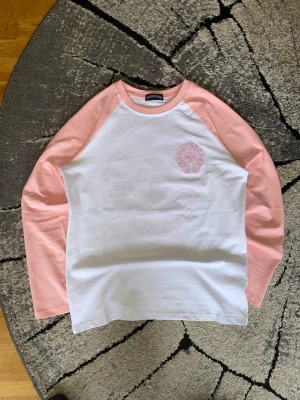 Chrome Hearts långärmad tröja - rosa/vit - || Säljer en Chrome Hearts long sleeve / baseball tee i rosa/vitt.  Ikoniskt kors-tryck på ryggen och mindre logga framtill. ||  || Skick: Använd, bra skick. Inget slitage, inga hål eller revor. Se bilder för exakt skick. || Storlek: L, passar även M. || || Snygg statement-piece som funkar både casual och mer uppstylat. Säljs då den inte kommer till användning. ||