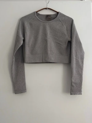 Grå ribbad croppad topp Aim'n - Säljer en grå croppad långärmad topp från Aim'n. Toppen är ribbad och har en rund halsringning. Perfekt för dig som gillar en enkel men stilren look. Materialet är mjukt och stretchigt, vilket gör den bekväm att bära.