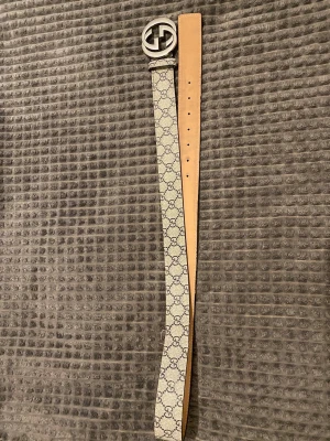 Gucci beige bälte med GG-mönstret  - Snyggt beige bälte från Gucci med klassiskt GG-mönster i blått och stor silverfärgad GG-logga somnar  spänne. Bältet har flera hål för justerbar passform och är gjort i skinn. Perfekt för att lyfta vilken outfit som helst.