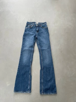 Blå bootcut jeans från Gina Tricot - Säljer ett par klassiska blå bootcut jeans från g perfect. Jeansen har fem fickor, normalhög midja och utsvängda ben. Tillverkade i slitstark denim med snygga kontrastsömmar. Perfekta för en avslappnad och trendig look.
