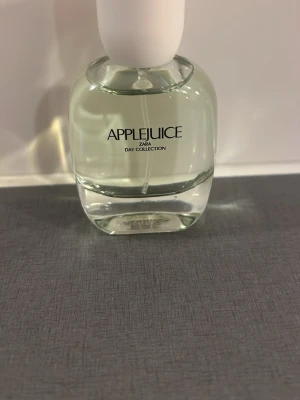 Zara Applejuice parfym - Fräsch parfym från Zara i doften Applejuice. Flaskan är rundad och genomskinlig med vit kork och svart text. Ingår i Day Collection och har en stilren, modern design som passar perfekt på sminkbordet.