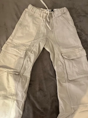 Cargo - Säljer ett par beige/vita cargo byxor från Pull & Bear. Oanvända. Prislapp fortfarande kvar. Storlek: XS/ 34. Original pris: 400kr