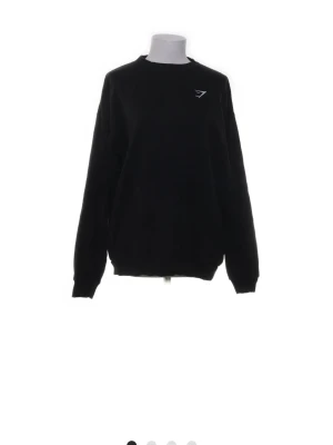 Svart sweatshirt från Gymshark - Säljer en svart sweatshirt från Gymshark med rund halsringning och diskret logga på bröstet. Tröjan har långa ärmar och ribbade muddar vid ärmslut och nederkant. Perfekt för gymmet eller till vardags