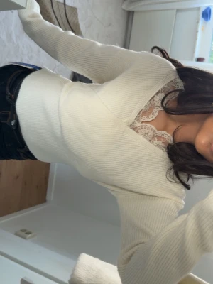 Vit omlottstickad tröja med spets - Supersnygg vit stickad tröja med omlottmodell och v-ringning dekorerad med spetskant. Tröjan har långa ärmar och ribbad struktur som ger en skön passform. 