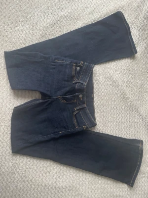Mörkblå bootcut jeans - Snygga mörkblå bootcut jeans med klassiska kontrastsömmar och fem fickor. Jeansen har en hög midja och är tillverkade i ett mjukt denimtyg som ger en skön passform. Perfekta för en avslappnad och trendig look.