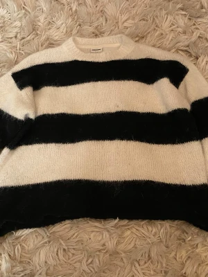 Randig stickad tröja  - Stickad tröja från vero Moda med breda svarta och vita ränder. Tröjan har rund halsringning och är gjord i ett mjukt, luddigt material som ger en mysig känsla. Perfekt för dig som gillar en avslappnad och trendig look.