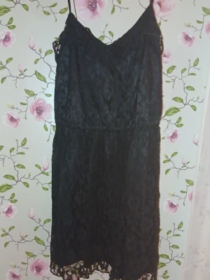 Svart spetsklänning med smala band - Säljer en svart kortklänning med tunna systerbarn axelband och vacker spetsdetalj över hela klänningen. Klänningen har en lätt v-ringad halsringning och är ärmlös, perfekt för dig som vill ha en stilren och elegant look.