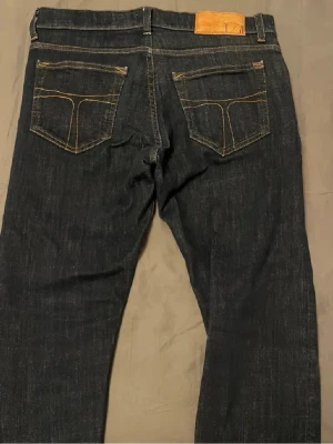 Mörkblå jeans från Tiger Of Sweden - Säljer ett par mörkblå jeans från Tiger Of Sweden med klassisk femficksmodell och kontrastsömmar. Jeansen har lite slima ben och normal passform, tillverkade i slitstarkt denimtyg av bomull. Perfekta för dig som gillar stilrena och tidlösa jeans. Storlek W29 men passar egentligen W30