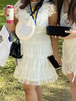 Studentklänning  - Söt vit kortklänning i spets med volangdetaljer och transparenta ärmar. Klänningen har en rund halsringning och är figurnära upptill med ett lätt utställd kjol. Perfekt för student eller sommarens tillfällen.