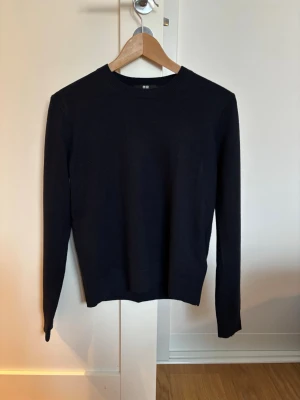 Marinblå kashmir tröja från Uniqlo - En stilren marinblå kashmir / cashmere tröja från Uniqlo med rund halsringning och långa ärmar. Tröjan har ribbade muddar vid ärmslut och nederkant. Mycket fint skick utan defekter.