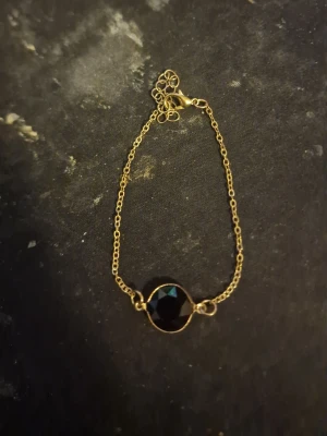 Guldarmband med svart pärla - Snyggt armband med tunn guldfärgad kedja och en stor, rund svart pärla i mitten. Låset är klassiskt och armbandet har en elegant och stilren design som passar perfekt till många olika looks.