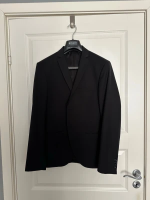 Svart kostym från Tiger of Sweden - Klassisk svart kostym från Tiger of Sweden med en kavaj och matchande byxor. Snygg passform och tidlös design. Använd fåtal gånger till studenten. Storlek: 48 (96)