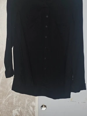 Blus - Svart blus från H&M. Använd en handfull gånger, så i stort sett som ny.  Hängt i en garderob de senaste åren, därav lite skrynklig. Har två fickor på bröstet.