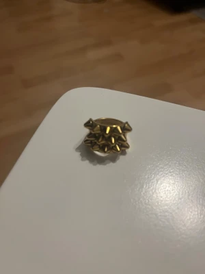 Guldfärgad chunky ring med nitar - Cool ring i guldfärgad metall med chunky design och flera spetsiga nitar runt hela ringen. Perfekt för dig som gillar statement-smycken och vill sticka ut med en edgy accessoar. Ringen har en bred form och glänsande finish.