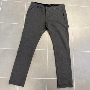 Grå kostymbyxor från Dondup - Snygga grå kostymbyxor från Dondup med smal passform och klassiska fickor fram. Byxorna har bälteshällor och stängs med dragkedja och knapp. Perfekta för en stilren look och tillverkade i ett mjukt, stretchigt material.