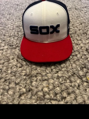 SOX  keps från New Era - Snygg snapback keps från New Era med SOX-brodyr framtill. Kepsen har vit front, röd skärm och mörkblå paneler på sidorna och bak. Klassisk rak skärm och broderad New Era-logga på sidan. Perfekt för dig som gillar sportig streetstyle.