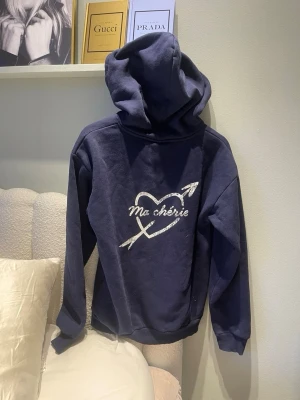 Mörkblå hoodie med tryck Ma chérie🤍 - Mörkblå hoodie med huva och trycket 'Ma chérie' i vitt på ryggen, dekorerat med ett hjärta och pil. Mindre tryck på bröstet. Mjuk och skön, perfekt för en avslappnad stil. Långa ärmar från Gina tricot storlek 158/164🤍🤍