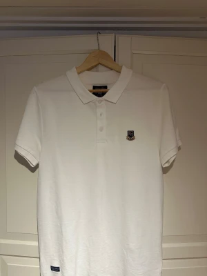 Vit pikétröja från Robbie Moor - Klassisk vit pikétröja från Robbie Moor med krage, knappar framtill. Den är i storlek S men passar ”mindre” medium. Använd vid endast 2 tillfällen.