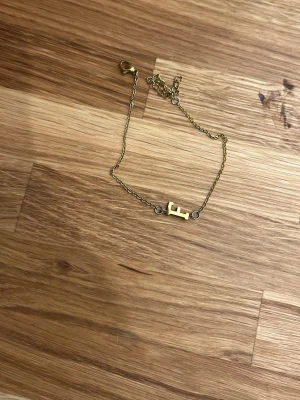 Guldfärgat armband med bokstav F - Snyggt armband i guldfärgad metall med en kedja och en bokstavsberlock i form av ett F. Perfekt accessoar för dig som vill ha något personligt och stilrent. Justerbar längd med karbinlås.