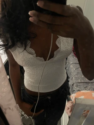 Vit spetsig croppad linnetopp - Säljer en vit croppad linnetopp med spetsdetaljer och v-ringad hals. Toppen har ett blommigt mönster i spetsen och är ärmlös, perfekt för en trendig och fräsch look. Passar snyggt till både jeans och kjol.