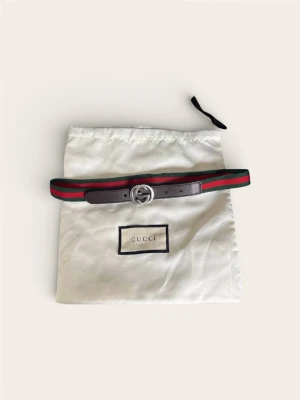 Gucci Bälte Barn – Klassisk Web (Grön/Röd) – Nyskick - Säljer ett exklusivt Gucci-bälte för barn. Detta är den ikoniska modellen med det elastiska gröna och röda bandet (Web) och detaljer i mörkbrunt läder. Skick: Nyskick! Bältet är endast använt vid ett enda tillfälle. Inga repor på spännet, lädret är fint och bandet är fräscht. Ser ut som nytt från butik.  Storlek: 75 cm. Justerbart tack vare steglös knäppning.  Pris: 799 kr (Nypris ca 3 000 kr).