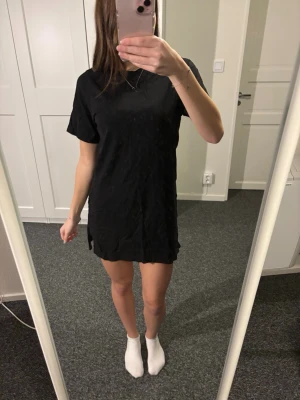 Svart t-shirtklänning Gina Tricot - Enkel och stilren svart t-shirtklänning från Gina Tricot. Klänningen har korta ärmar, rak passform och rund halsringning. Perfekt basplagg som är lätt att styla med accessoarer. Tillverkad i mjuk bomull för skön känsla.